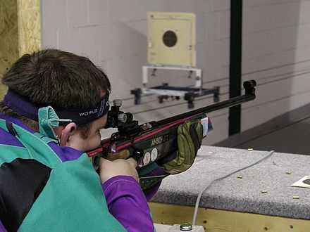 Ein Sportschütze liegt im Anschlag und zielt mit einem Luftgewehr auf eine Zielscheibe in einer Indoor-Schießanlage.