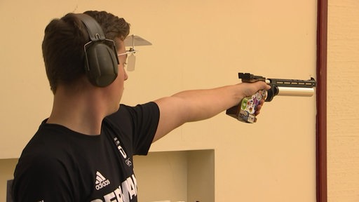 Ein junger Schütze zielt mit einer Luftpistole, trägt Gehörschutz und Schutzbrille während des Trainings.